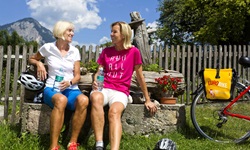 Zwei Radfarerinnen machen auf einer Bank in Tirol Pause.