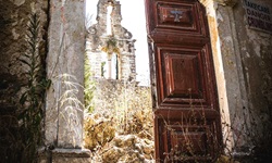 Ein halb offen stehendes Holzportal gibt den Blick auf eine steinerne Kirchenruine frei.