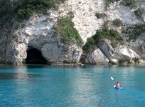 Ein Mann in einem Kanu auf dem Meer, der in Richtung einer Höhle der Ionischen Inseln paddelt