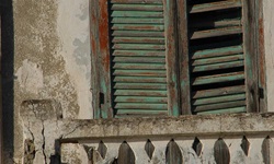 Detailbild eines grünlichen, alten, kaputten Fensterladens mit einem weißen Geländer, das ebenfalls kaputt ist