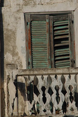 Detailbild eines grünlichen, alten, kaputten Fensterladens mit einem weißen Geländer, das ebenfalls kaputt ist