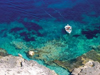 Ein Boot mit einem Mann in einer Bucht mit türkisblauem Wasser und Blick auf den Untergrund