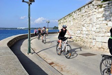Eine Radlergruppe fährt auf einer asphaltierten Straße am tiefblau schimmernden Meer vor der istrischen Küste entlang.