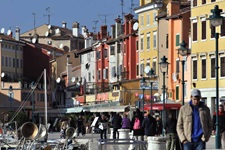 Touristen flanieren durch eine von bunten Häusern geprägte Gasse am Hafen von Rovinj.
