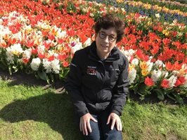 Eine Frau mit kurzen braunen Haaren und Brille sitzt an einem blühenden Blumenfeld aus weißen Hayzinthen und roten Tulpen