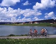 Eine Gruppe mit vier Radfahrern passiert einen der zahlreichen Seen, an denen die Jura-Route vorbeiführt.