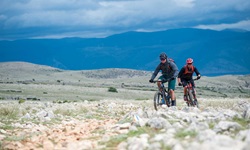 Zwei Mountainbiker fahren auf einem steinigen Naturweg über eine Insel der Kvarner Bucht.