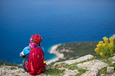 Eine Mountainbikerin mit rotem Helm und Rucksack sitzt auf einer Felsklippe und schaut hinab auf die Kvarner Bucht.