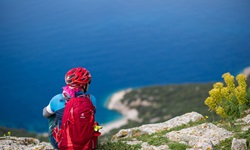Eine Mountainbikerin mit rotem Helm und Rucksack sitzt auf einer Felsklippe und schaut hinab auf die Kvarner Bucht.