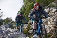 Zwei Mountainbiker - eine Frau und ein Mann - biken auf einem von Steinmäuerchen eingerahmten Naturweg über eine Insel der Kvarner Bucht.