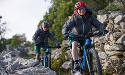 Zwei Mountainbiker - eine Frau und ein Mann - biken auf einem von Steinmäuerchen eingerahmten Naturweg über eine Insel der Kvarner Bucht.