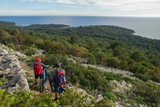 Zwei Mountainbiker - ein Mann und eine Frau - haben auf einem von Mäuerchen eingerahmten, grob geschotterten Weg Halt gemacht und genießen den Ausblick über die Kvarner Bucht.