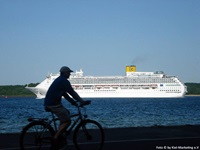 Ein Radfahrer fährt an der Ostseeküste entlang und im Hintergrund ist ein Krauzfahrtschiff auf dem Meer zu sehen