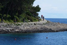 Eine Gruppe Radfahrer auf der Insel Losinj fährt auf einem asphaltierten Radweg am tiefblauen Meer der Kvarner Bucht entlang.