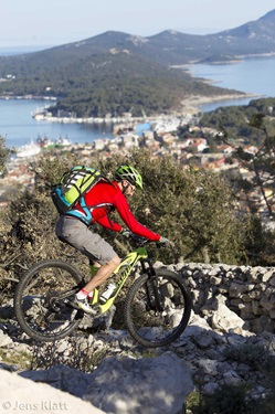 Ein Mountainbiker mti roter Jacke fährt einen felsigen Trail in Kroatien hinab