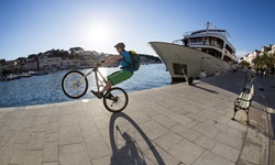 Ein Mountainbiker mit grüner Hose macht einen Wheelie an einer Hafenpromenade in der Kvarner Bucht in Kroatien