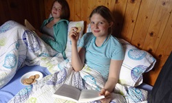 Zwei Kinder sitzen im Bett, essen Kekse und lesen ein Buch auf dem Schiff Andela Lora