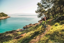 Ein Mountainbiker fährt auf einer Kvarner-Bucht-Insel einen parallel zum Meer verlaufenden Naturweg hinunter.