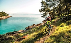 Ein Mountainbiker bei einer rasanten Abfahrt auf einem Naturweg, der parallel zum türkisblauen Meer der Kvarner Bucht verläuft.