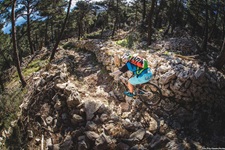 Ein Mountainbiker mit buntem Rucksack fährt auf einer Insel der Kvarner Bucht einen von zwei Mäuerchen eingerahmten, anspruchsvollen Weg mit großen Steinen hinunter.