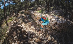Ein Mountainbiker mit buntem Rucksack fährt auf einer Insel der Kvarner Bucht einen von zwei Mäuerchen eingerahmten, anspruchsvollen Weg mit großen Steinen hinunter.