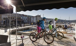 Zwei Mountainbiker erreichen nach erfolgreich absolvierter Tagesetappe den Hafen und bewältigen die letzten Meter, die sie noch vom Schiff trennen.