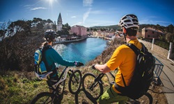 Zwei Mountainbiker - ein Mann und eine Frau - genießen den Ausblick auf den Hafen von Veli Losinj und die Kirche des Heiligen Anton.
