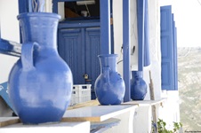 Blaue Keramikvasen vor einem typischen, in Weiß und Blau gehaltenen Haus auf den Kykladen.