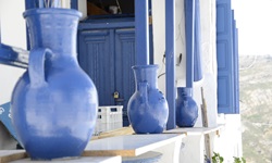 Blaue Keramikvasen vor einem typischen, in Weiß und Blau gehaltenen Haus auf den Kykladen.