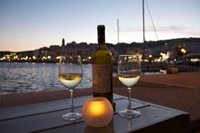 Eine Tisch mit zwei Gläsern griechischem Wein, einer Weinflasche und einem Teelicht in der Abenddämmerung am Hafen