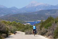 Eine Radlerin fährt auf der Kykladeninsel Poros auf einem asphaltierten Radweg dem Meer entgegen.