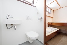 Eine Zwei-Bett Kabine mit einem erhöhtem Einzelbett vom Badezimmer mit WC und Waschbecken aus fotografiert