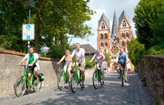 Eine Radlergruppe verlässt über eine Brücke die Limburger Fußgängerzone - im Hintergrund der prächtige Limburger Dom.