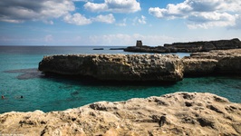 Beeindruckende Felsküstenlandschaft des Salento, im Hintergrund ist die Ruine eines Turmes zu erkennen.