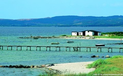 Blick auf einen Holzsteg mit Leiter zu einem Haus und Booten im Meer bei Roskilde in Dänemark