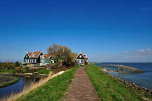 Ein kleiner Deich in Richtung eines kleinen Dörfchens entland des Ijsselmeeres
