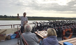 Ein Reiseleiter erläutert zwei Passagieren auf dem Sonnendeck den weiteren Ablauf des Tages. Neben ihm warten die aufgereihten Fahrräder auf ihren Einsatz.