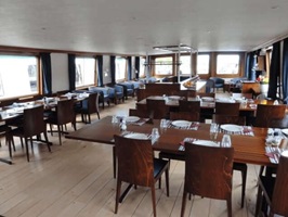 Blick zum eingedeckten Restaurant, der Bar und dem Salon mit blau bezogenen Sesseln der MS Lena Maria