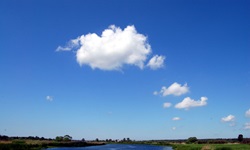 Strahlend blauer Himmel mit einigen weißen Wattewölkchen über einem Flusslauf.