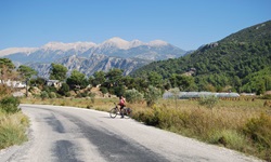 Ein Fahrradfahrer posiert auf einer Straße für die Kamera - im Hintergrund sind beeindruckende Berggipfel, die mit Schnee bedeckt sind zu sehen