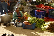 Eine Frau sitzt auf dem Boden vor ihrem Obst und Gemüse, das sie auf dem Markt verkauft