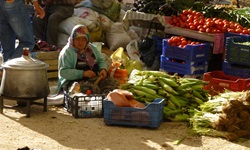 Eine Frau sitzt auf dem Boden vor ihrem Obst und Gemüse, das sie auf dem Markt verkauft