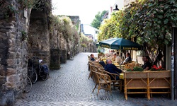 Touristen und Einheimische sitzen unter grünen Sonnenschirmen in einem Straßencafé in der Altstadt von Maastricht.