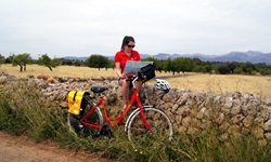 Eine Radlerin hat es sich auf Mallorca auf einem Steinmäuerchen bequem gemacht und studiert ihr Kartenmaterial.