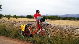 Eine Radlerin hat es sich auf Mallorca auf einem Steinmäuerchen bequem gemacht und studiert ihr Kartenmaterial.