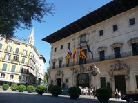 Das Mallorquinische Rathaus in Palma mit vier Fahnen und einer Uhr - im Hintergrund die Spitze der Kathedrale