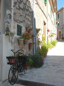 Eine Gasse auf Mallorca die mit einem alten bepflanzten Fahrrad und Töpfen an der Wand sowie auf dem Boden