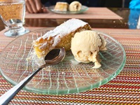 Ein schön angerichteter Glasteller mit einem Dessertlöffel, einem Stück Mandelkuchen und einer Kugel Vanilleeis