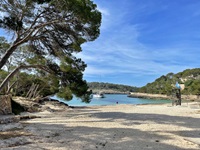 Blick auf den Strand und die Bucht, in der ein kleines Schiff liegt, im Naturpark Mondrago auf Mallorca