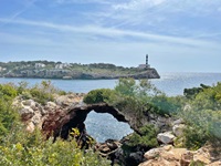 Blick zu über ein Bucht mit einer natürlichen Steinbrücke zum Leuchtturm Portocolom auf Mallorca